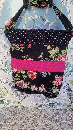 A black Angelica purse with a pink floral pattern and a hot pink and white polka-dots on black fabric stripe, displayed against a floral background.