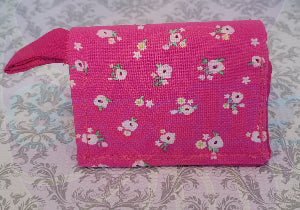 A hot pink wallet with white flowers printed on it, displayed on a patterned background.