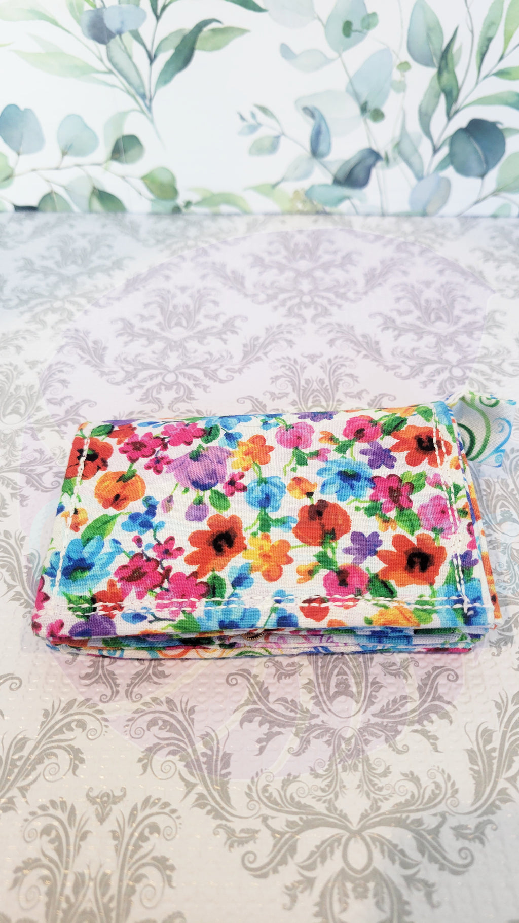 Colorful floral-patterned fabric on a textured surface with decorative background. Wallet is closed.
