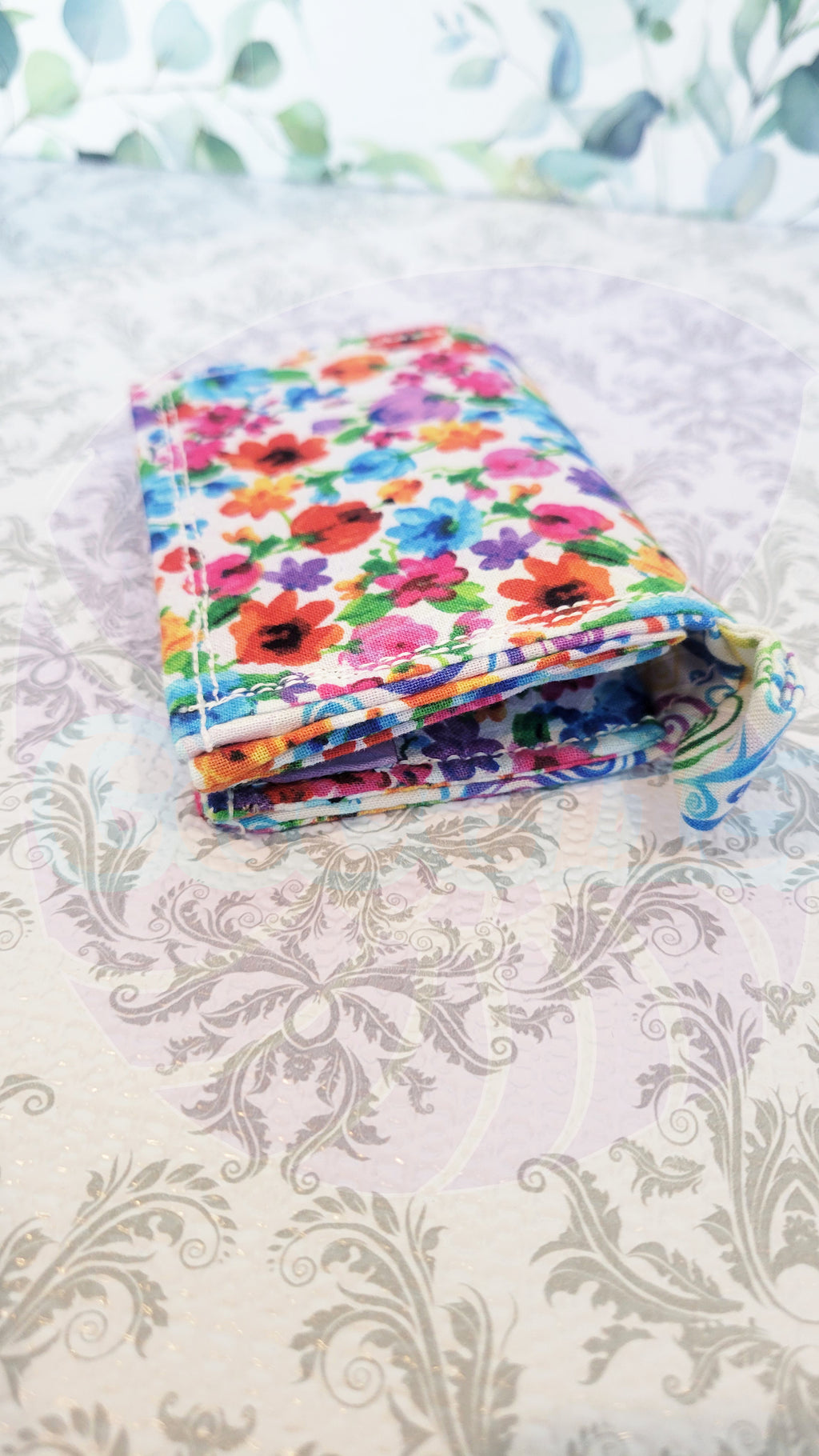 Colorful floral wallet on a patterned surface. Wallet is showing its side hook.