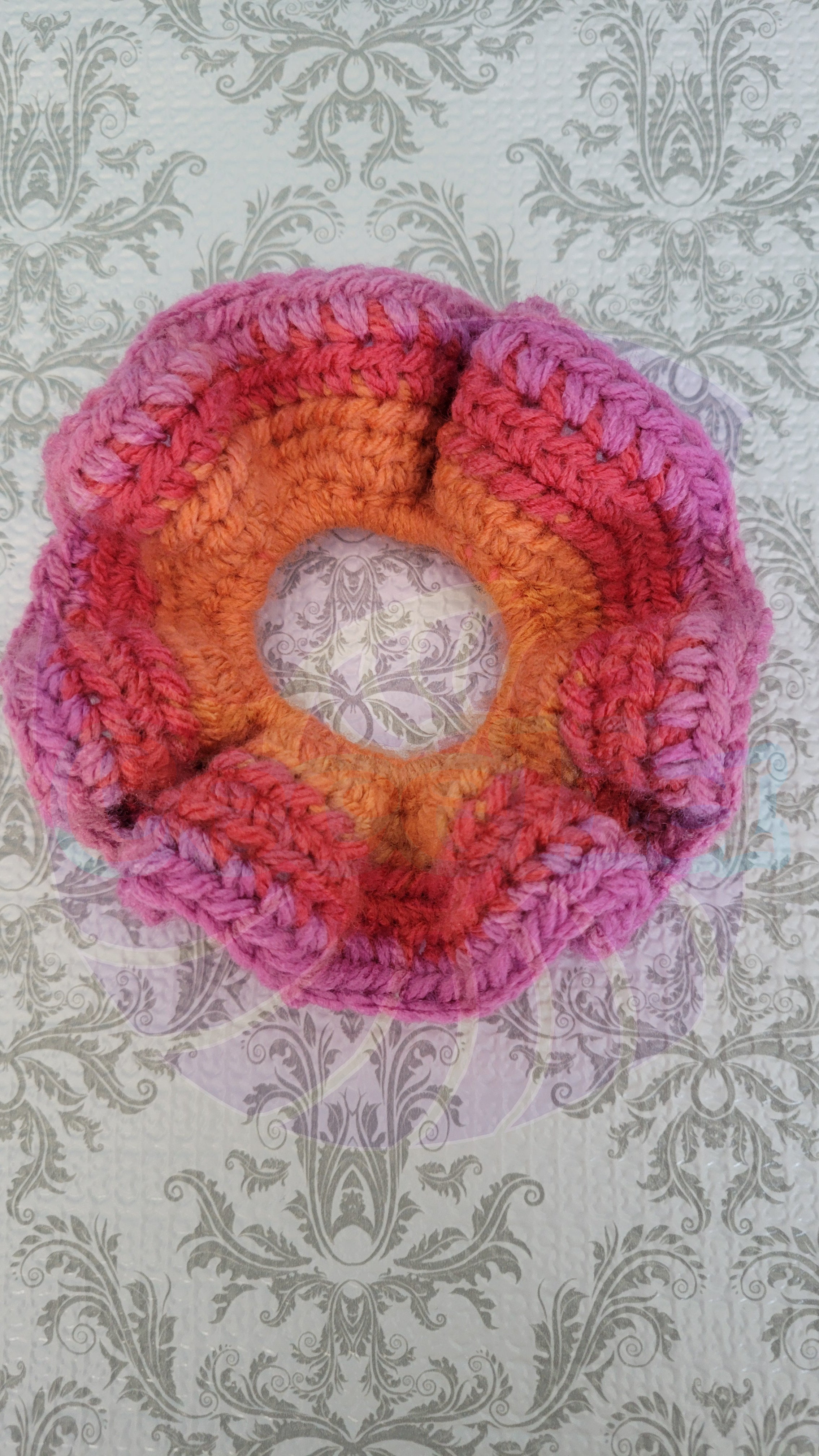 Crocheted flower in pink, orange, and purple on a patterned background