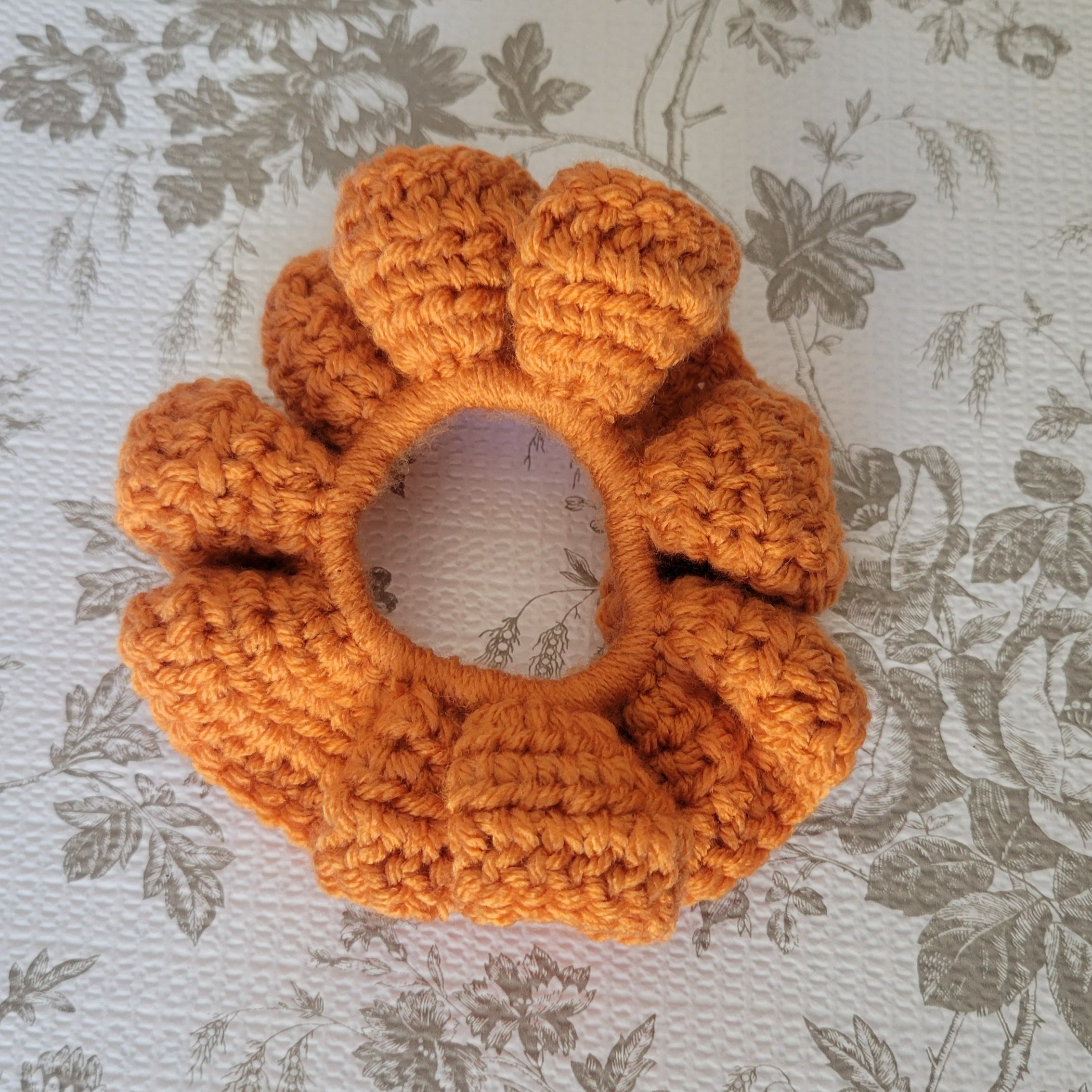 Orange crochet scrunchie on a floral-patterned fabric background
