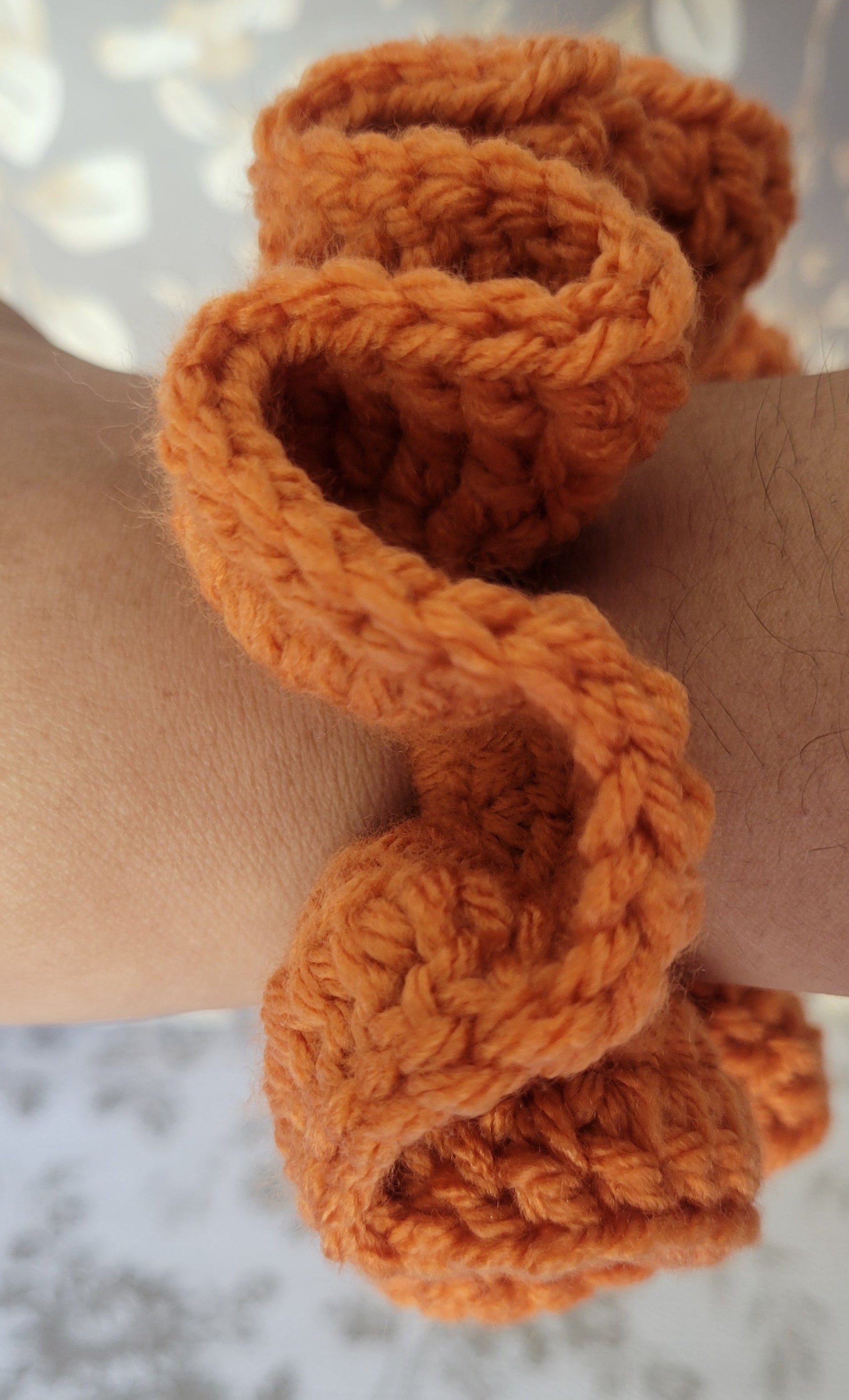 Orange knitted scrunchie on a wrist with a blurred background