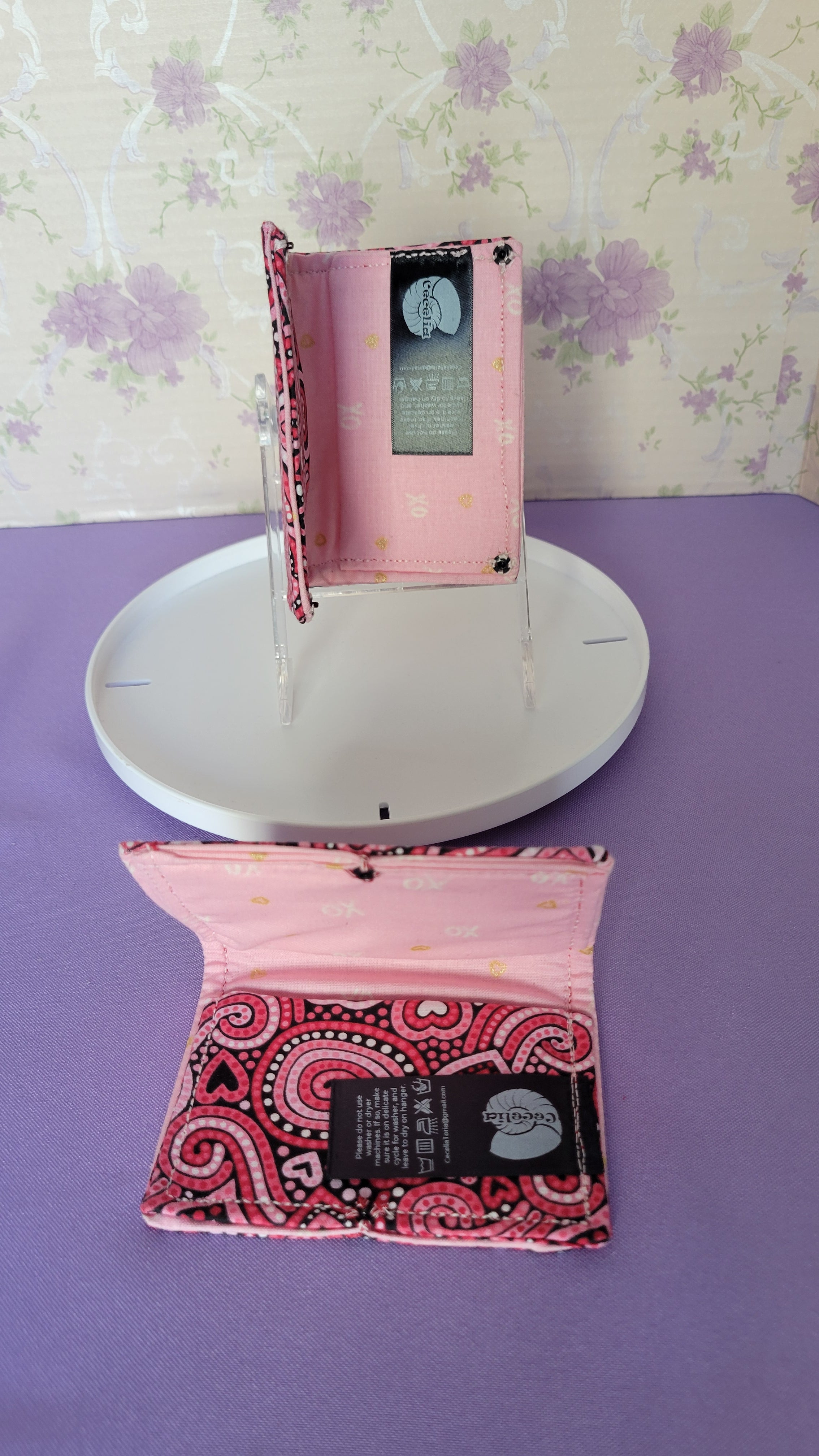 Two Javier wallets with a ripple effect of hearts in a selection of colors pink, white, red and black. They are placed parallel with one on a turning table.