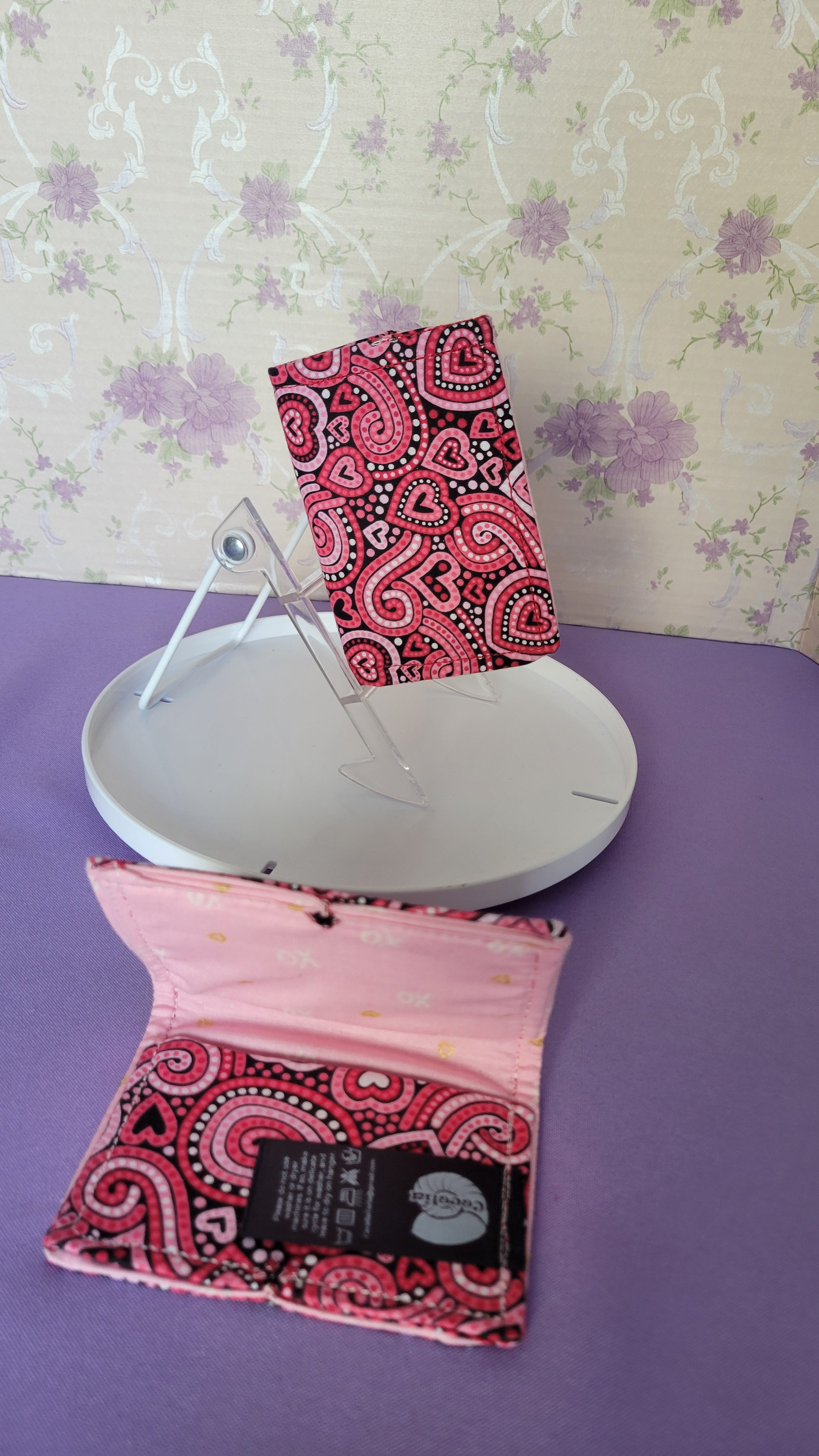 Two Javier wallets with a ripple effect of hearts in a selection of colors pink, white, red and black. They are placed parallel with one on a turning table.