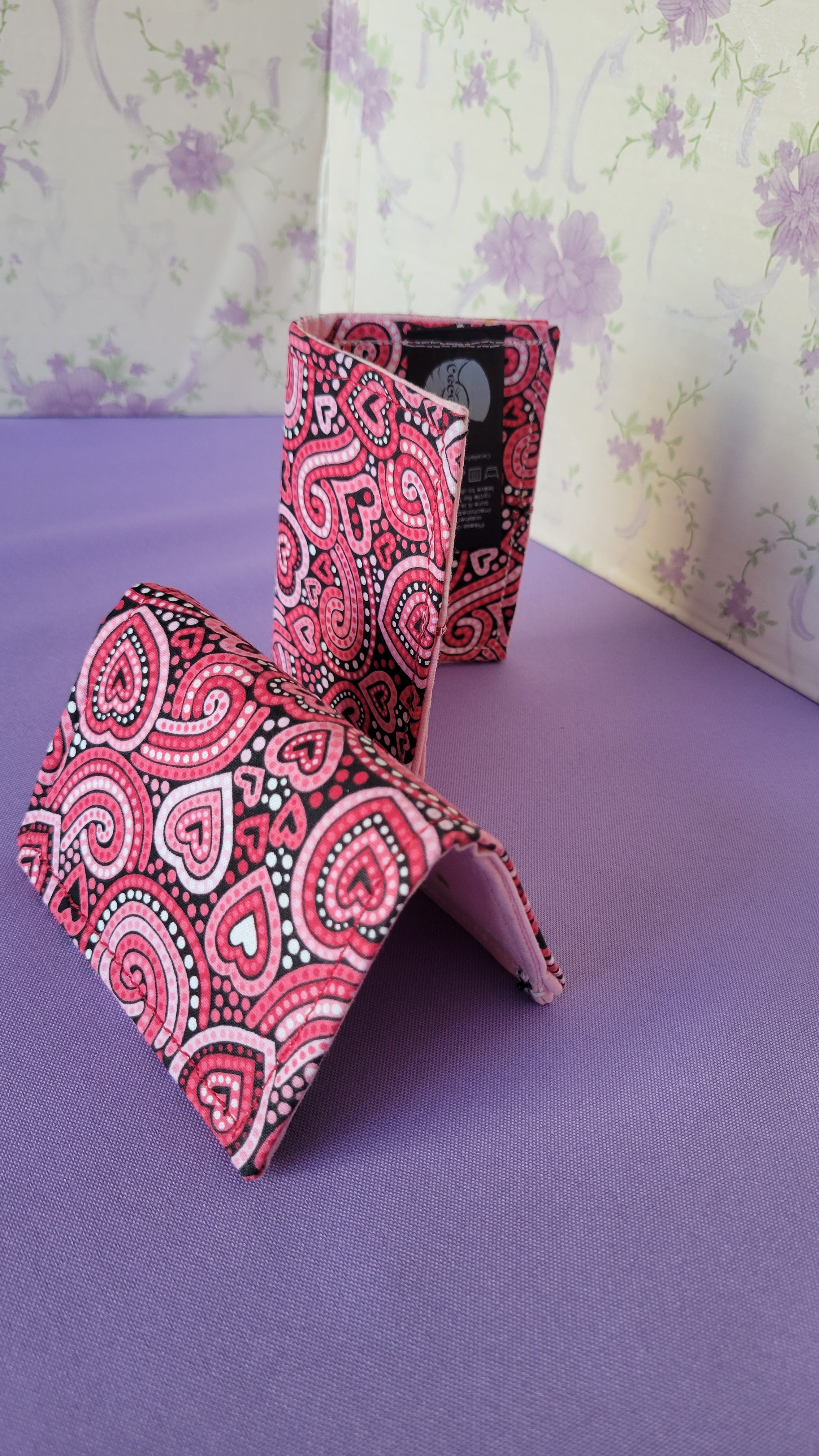 Three Javier wallets with a ripple effect of hearts in a selection of colors pink, white, red and black. They are placed parallel with one on a turning table.